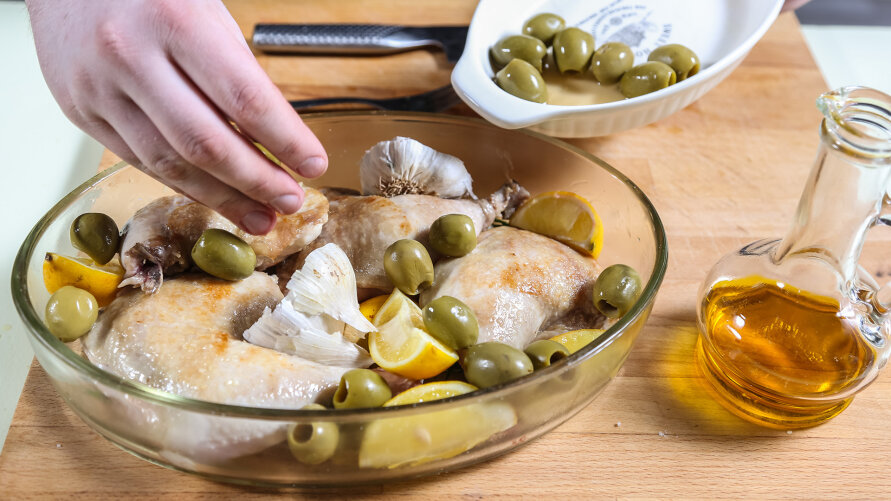 Ułóż w naczyniu żaroodpornym kurczaka, obłóż go czosnkiem, cytryną i oliwkami